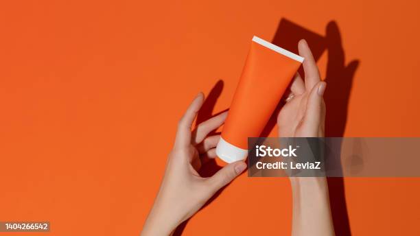Female Hands Holding Blank Orange Plastic Cosmetic Tube On Orange Backgroundmockup Stock Photo - Download Image Now