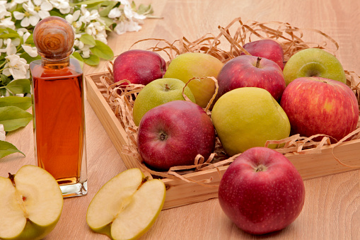 A bottle of apple cider vinegar, a box of apples, branches of flowering white and red apple trees on a light background.