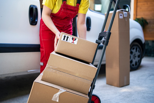 Delivery woman loading parcels on push cart.