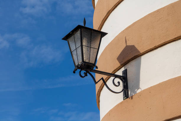 old, ornate iron street lantern hangs hangs on a round tower with sandstone and plaster facade in rings before strong blue sky