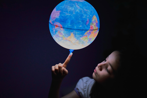 Little girl looking interested in the dark at an illuminated earth globe