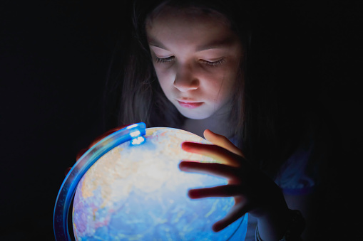 Little girl looking interested in the dark at an illuminated earth globe