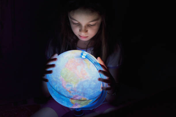 petite fille regardant dans l’obscurité un globe terrestre illuminé - elementary age focus on foreground indoors studio shot photos et images de collection