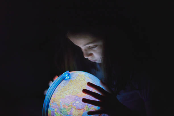 petite fille regardant dans l’obscurité un globe terrestre illuminé - elementary age focus on foreground indoors studio shot photos et images de collection