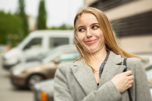 fun blond young confused woman at parking grimacing outdoors smiling, looking aside