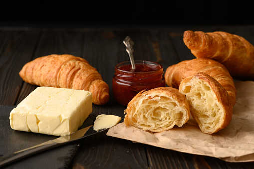 Freshly baked croissants with berries jam and butter, dark wooden background, selective focus