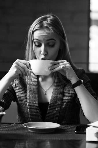 young blond woman with cup of tea in cafe, monochrome