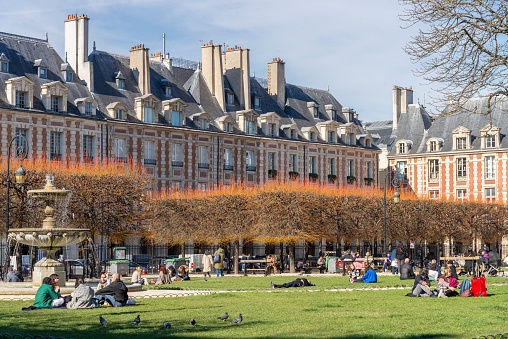 Group of young people enjoying themselves on the lawn during a sunny day in Place des Vosges in Le Marias district, Paris, France.