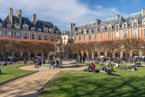 Group of young people enjoying themselves on the lawn during a sunny day in Place des Vosges in Le Marias district, Paris, France.
