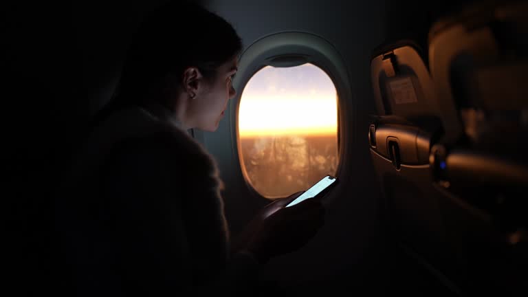 Woman using smartphone and looking through the window in an airplane