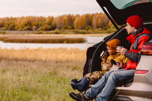 Family traveling by car having rest and looking at beautiful Fall landscape Father and son drinking tea sitting in car trunk road trip stock pictures, royalty-free photos & images