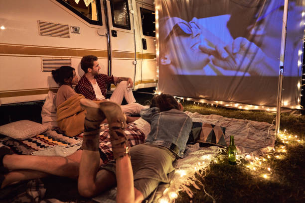 Happy group of young cheerful people watching a movie on camping site stock photo