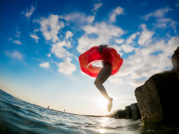 une fille dans une bouée de sauvetage gonflable saute dans l’eau de mer. activités de plage d’été. grand angle go pro - floatation device flash photos et images de collection