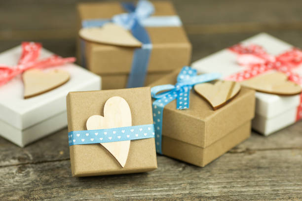 Bright spring gift boxes on a wooden table. They are decorated with pink and blue ribbons and wooden figures in the shape of a heart.
