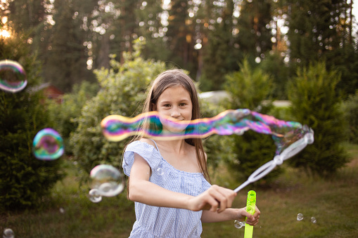 Girl launches soap bubbles on the street. Background of green trees