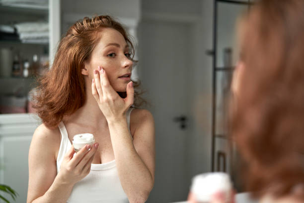 Woman using face cream in the bathroom stock photo