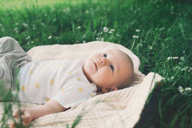 lindo bebé feliz acostado en una manta sobre hierba verde en verano al aire libre. bebé descalzo de 3 meses en la naturaleza. concepto familiar e infantil de estilo de vida eco sostenible. - baby mother summer park fotografías e imágenes de stock