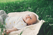 Cute happy baby lying on blanket on green grass at summer outdoors. 3 months old barefoot baby on nature. Family and childhood concept of  eco sustainable lifestyle.