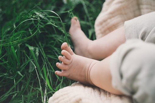 Baby tiny cute feet in green grass outdoors. Baby lying on blanket at summer on nature.