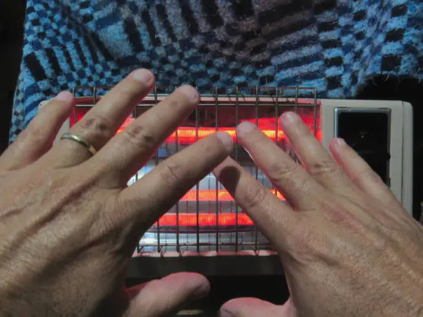 Hands of a middle-aged married man warming himself in front of the electric heater during a cold night - POA, SAO PAULO, BRAZIL.