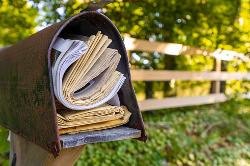 Yellowing newspapers fill an old mailbox after being exposed to weather.