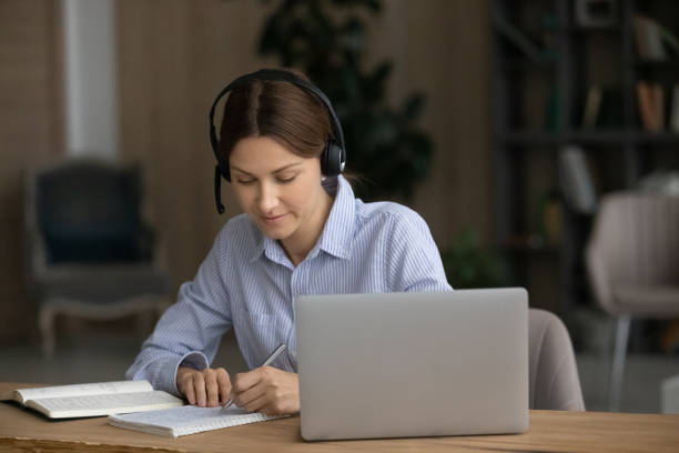 istock Attentive woman listen audio course noting studying use modern tech 1404289769