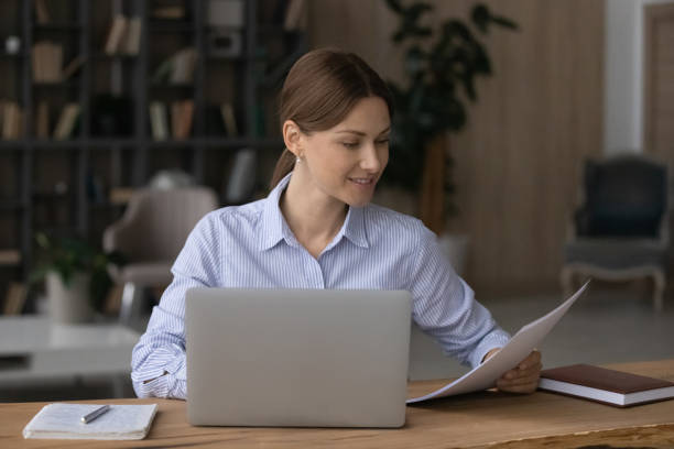 istock Businesswoman sit at desk with laptop holding papers read documents 1404289770
