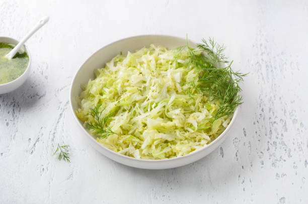 istock Steam white cabbage in a white ceramic bowl with herbs and green sauce on a light blue background, top view. Delicious diet food 1404289962