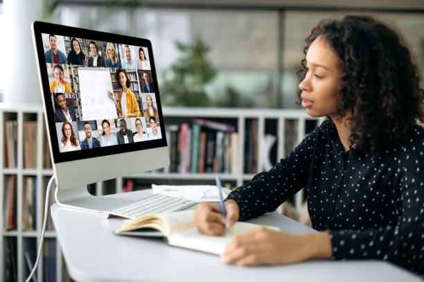 istock Online learning. Smart african american curly girl, sits at a desktop in front of a computer screen, concentrated watches and listens to an online lecture, takes notes, gain knowledge 1404293214