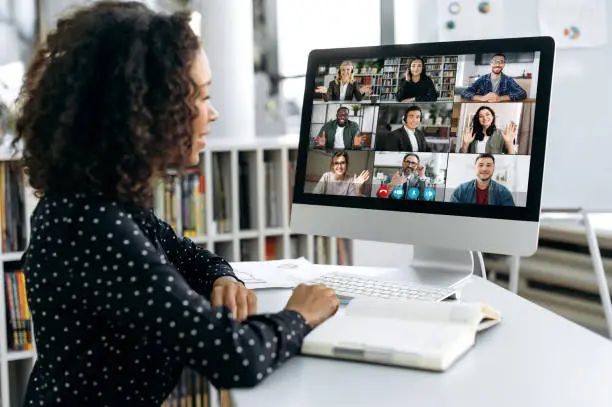 Photo of African american business woman, sits in front of a computer screen, talks via video link with international colleagues, employees, discusses a future project, perspective, business strategy, plan