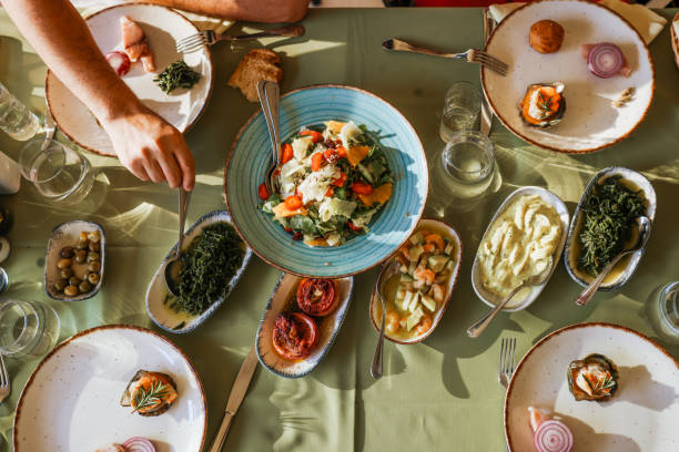 Couple Eating Lunch with Fresh Salad and Appetizers Closeup of multi generation family having Thanksgiving dinner. There are two mid adult couple and a mid 20's couple having a big feast, sharing food and love. Raki and meze meze stock pictures, royalty-free photos & images