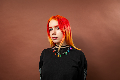 Studio portrait of an 18 year old woman with brightly dyed hair on a brown background
