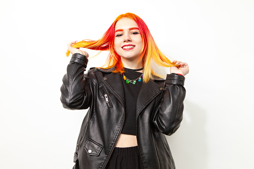 Studio portrait of an 18 year old woman with brightly dyed hair in a black leather jacket on a white background