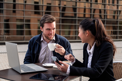 young businessman chats about work with his female coworker over coffee on a terrace in the financial district, concept of entrepreneurship and business