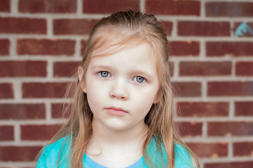 Elementary age little girl with blonde hair has a blank expression staring into camera.  Pretty girl is sad