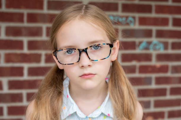 portrait of a little girl with glasses and a red ball outdoors looking at the camera
