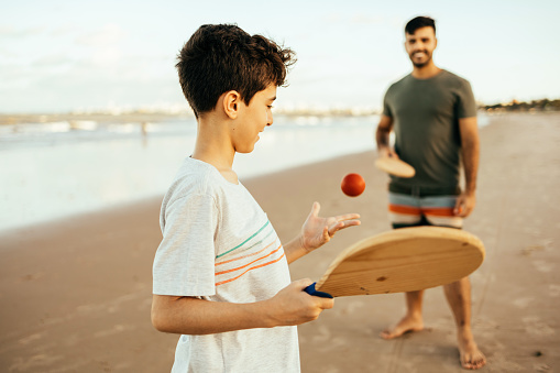 Father and son having fun on the beach during summer vacation playing beach tennis