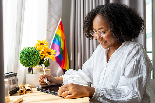 African American girl is working at home with LGBTQ rainbow flag in her table for coming out of closet and pride month celebration to promote sexual diversity and equality homosexual orientation