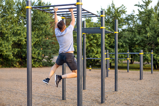 A man trains in an open area and pulls himself up on a horizontal bar. Outdoor fitness gym
