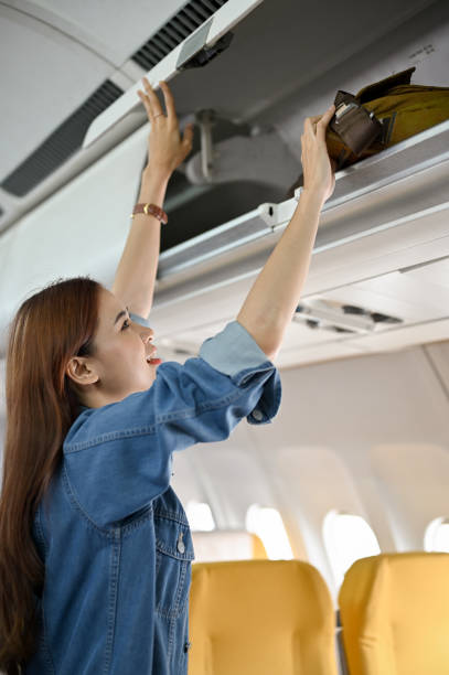 頭上のロッカーや頭上のコンパートメントにバッグを置く美しい若いアジア人女性。 - commercial airplane airplane cabin passenger ストックフォトと画像