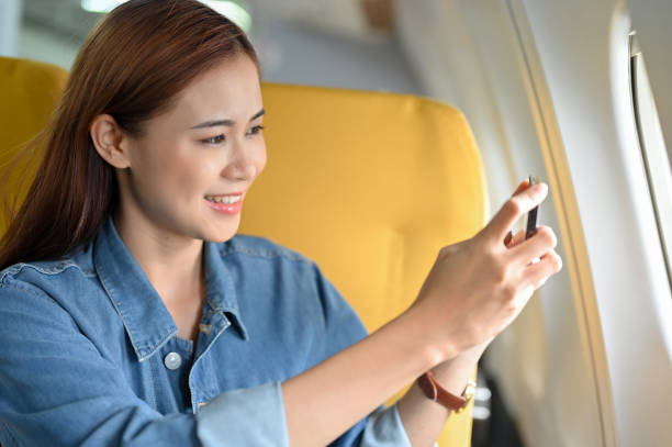 飛行機で旅行する美しい若いアジア人女性、スマートフォンで空の写真を撮る。 - commercial airplane airplane cabin passenger ス��トックフォトと画像