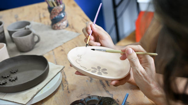 A female hands making a ceramic plate, painting and drawing beautiful flowers on ceramic plate with acrylic colour. cropped image