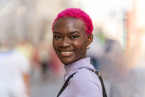 Portrait of a african young woman with short pink hair turning to smile to the camera