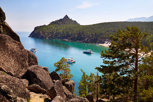 Picturesque seascape. Yachts in a bay with turquoise water color. Around the rocks, huge stones and coniferous forest. Untouched nature, rest in a wild place.