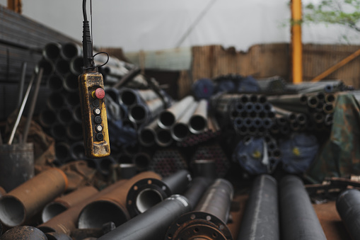 Remote control of a lifting crane hanging in the foreground against a whole inventory of ductile iron pipes and parts