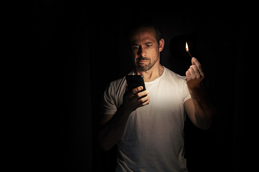 Man looking at his cell phone with a match in the dark. Blackout concept. Selective focus.