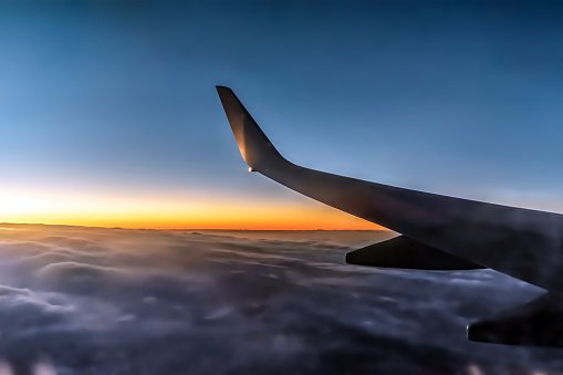 Airplane wing at dusk during sunrise. Dark silhouette of a part of the plane above the clouds against the background of an orange horizon