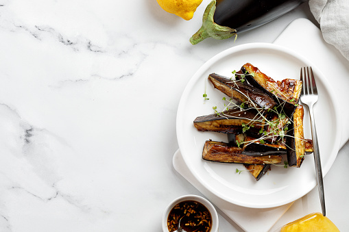 Glazed Fried eggplant sticks with sauce, honey, microgreens on white plate and marble background, delicious vegetarian dish. Top view, copy space