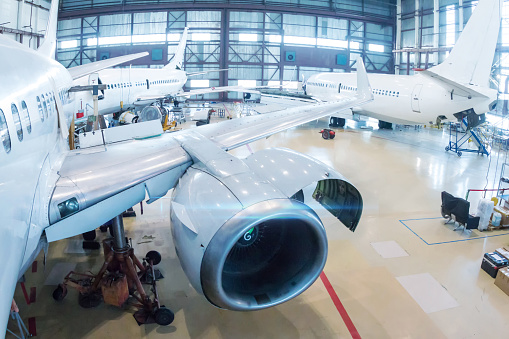 White passenger airliners in the hangar. Aircrafts under maintenance. Checking mechanical systems for flight operations