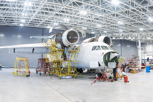 White transport aircraft in the hangar. Airplane under maintenance. Checking mechanical systems for flight operations
